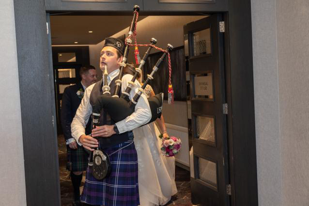 Scottish Piper Hire playing bagpipes for bride and groom marching into reception. 
