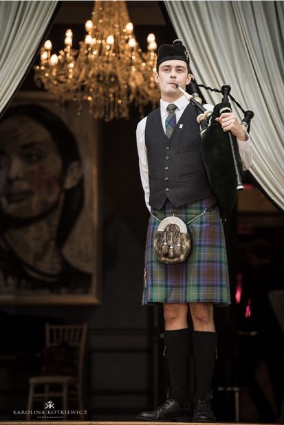 Scottish Piper Hire standing with bgapipes in traditional dress at the top of a set of stairs.