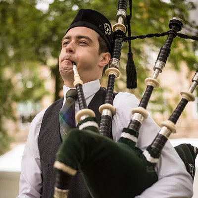 a close up of Scottish Piper Hire playing bagpipes outside in front of a tree.