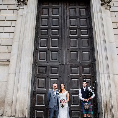 Scottish Piper Hire playing bagpipes whilst standing outside St Pauls cathedral. Playing beside the Bride and Father of the Bride. 